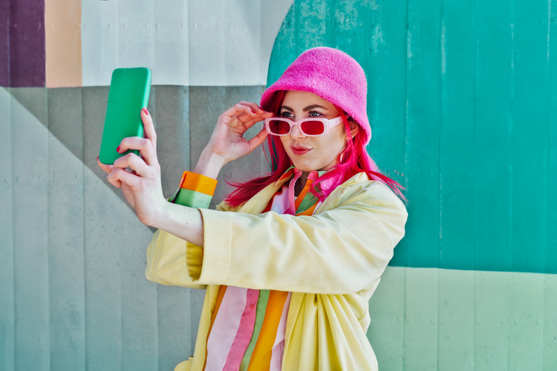 Frau mit bunter Kleidung und rosa Haaren macht ein Selfie